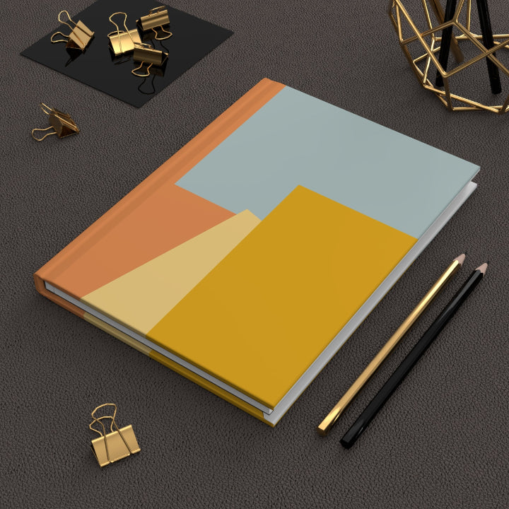 Notebook with geometric color blocks on a dark surface with office supplies.