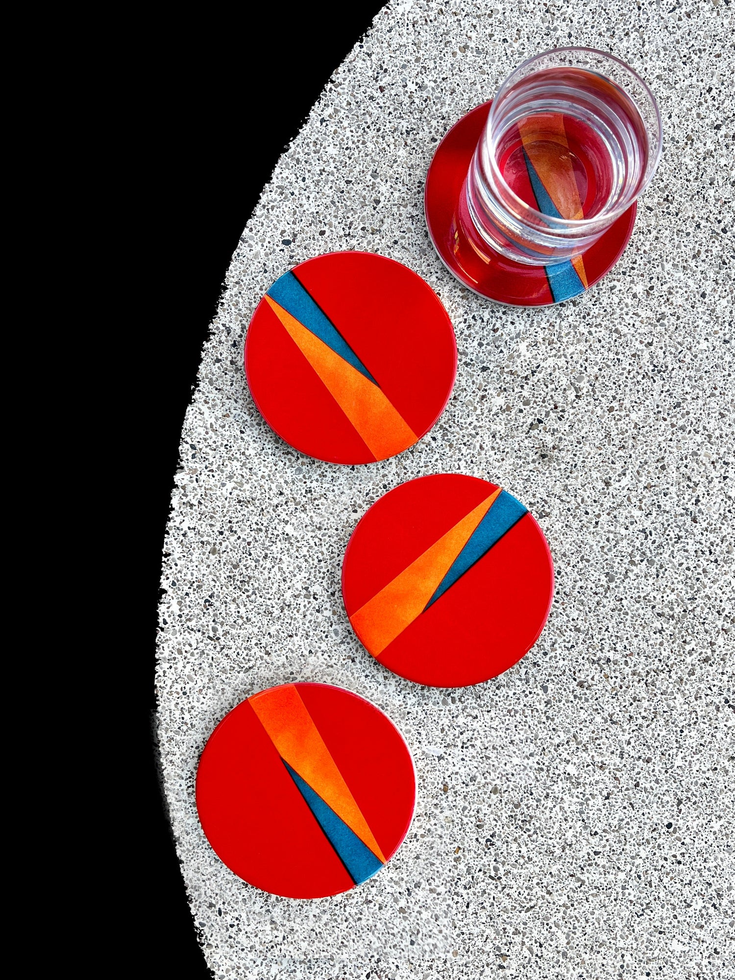 Set of three red circular coasters with orange and blue stripes on a textured surface.