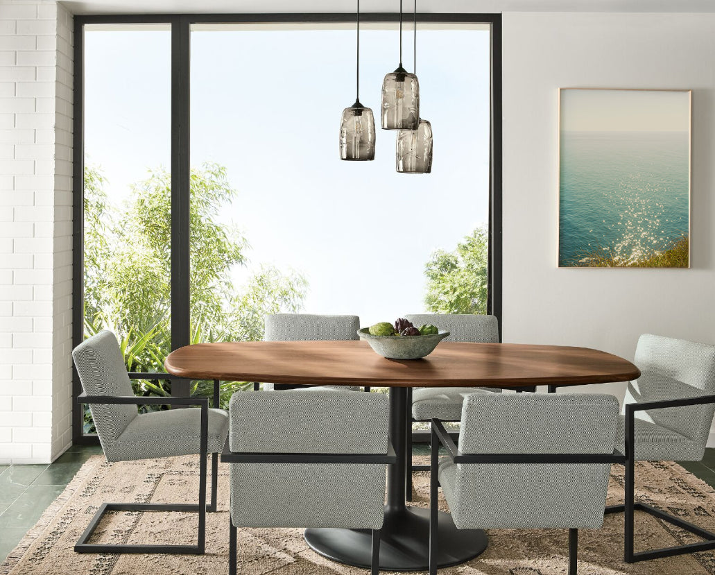 Dining room with a wooden table and gray chairs near a large window with a view of greenery. Sold at Room and Board