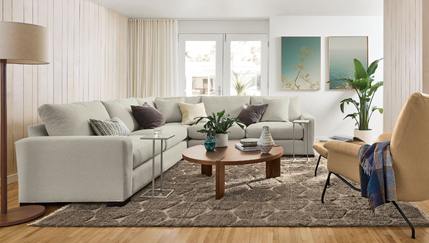 Modern living room with a gray sectional sofa, wooden coffee table, and decorative elements at Room and Board.